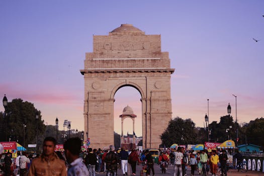 A bustling scene at India Gate with a vibrant crowd under a colorful sunset sky.