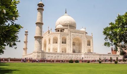 Iconic Taj Mahal showcasing its white marble beauty and lush gardens on a sunny day.