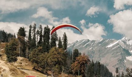 Thrilling paragliding above Manali's scenic landscape with majestic Himalayan mountains.