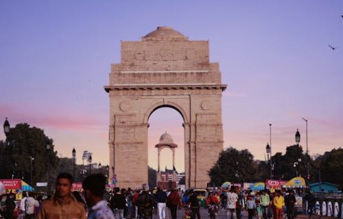 A bustling scene at India Gate with a vibrant crowd under a colorful sunset sky.